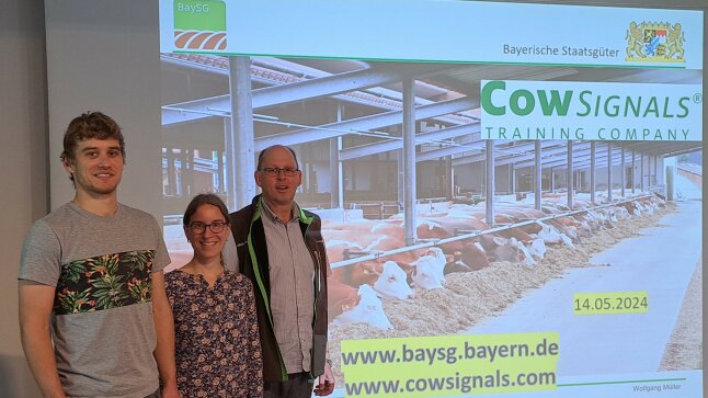 Drei Personen vor einer Leinwand mit Kühen und einem Schriftzug: CowSignals Training Company