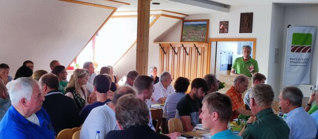 Viele Personen sitzen im Saal und hören einem Redner zu