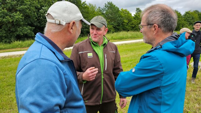 Drei Personen auf Wiese in Diskussion