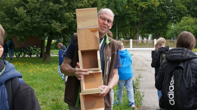 Ein Mann steht auf einer grünen Wiese mit vielen Schwalbenhäusern auf dem Arm