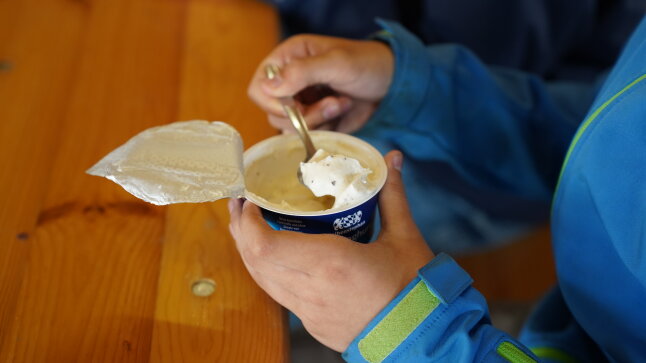 ein Joghurtbecher mit einer Kinderhand und einem Löffel