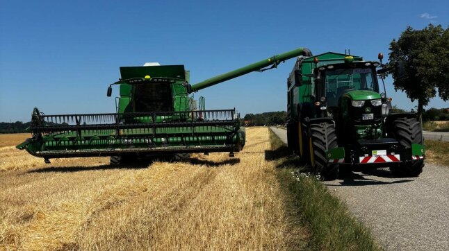 Ein Mähdrescher steht auf einem gedroschenen Weizenfeld neben einem großen Traktor