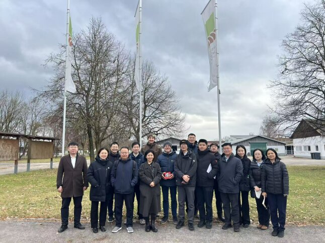 Eine Gruppe an Menschen stehen vor einer Wiese und 3 Fahnen