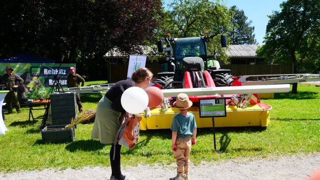 im Vordergrund eine Mama erklärt einem Kind einen Traktor