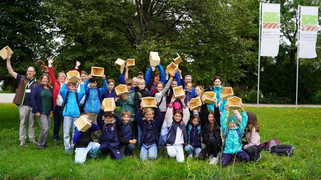 Gruppenbild mit Schülern auf einer Wiese mit Schwalbenhäusern aus Holz