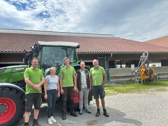 4 Männer und eine Frau stehen vor einem grünen Fendt Traktor und lächeln in die Kamera